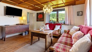 Un salon avec un plafond en bois, une télévision, un canapé et une table sur laquelle est posée une bougie.