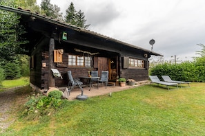 Una cabaña rústica de madera con un patio, mobiliario exterior y una antena parabólica.