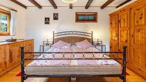 A bed with a metal frame, wooden headboard, and floral bedding. There are two bedside tables with lamps. The room has wooden walls and a wooden cabinet. - Holiday Home 'Blockhaus Paepke' with Private Terrace and Private Garden (Mühlenbach)
