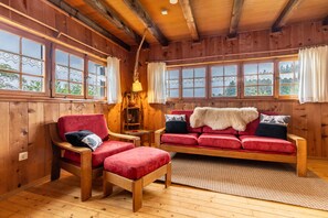 Ein Holzblockhaus-Interieur mit einem roten Sofa, einem Holzstuhl und einer Lampe.