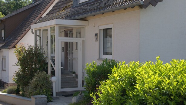Une maison dotée d’un porche abrité, d’un escalier apparent et d’un jardin bien entretenu.