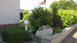 Un jardin aménagé avec un banc en pierre, une petite fontaine et une variété d’arbustes.