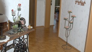 Un couloir doté d’un plancher en bois, une machine à coudre, une table ornée d’objets décoratifs et un mur agrémenté de motifs floraux et d’inscriptions.