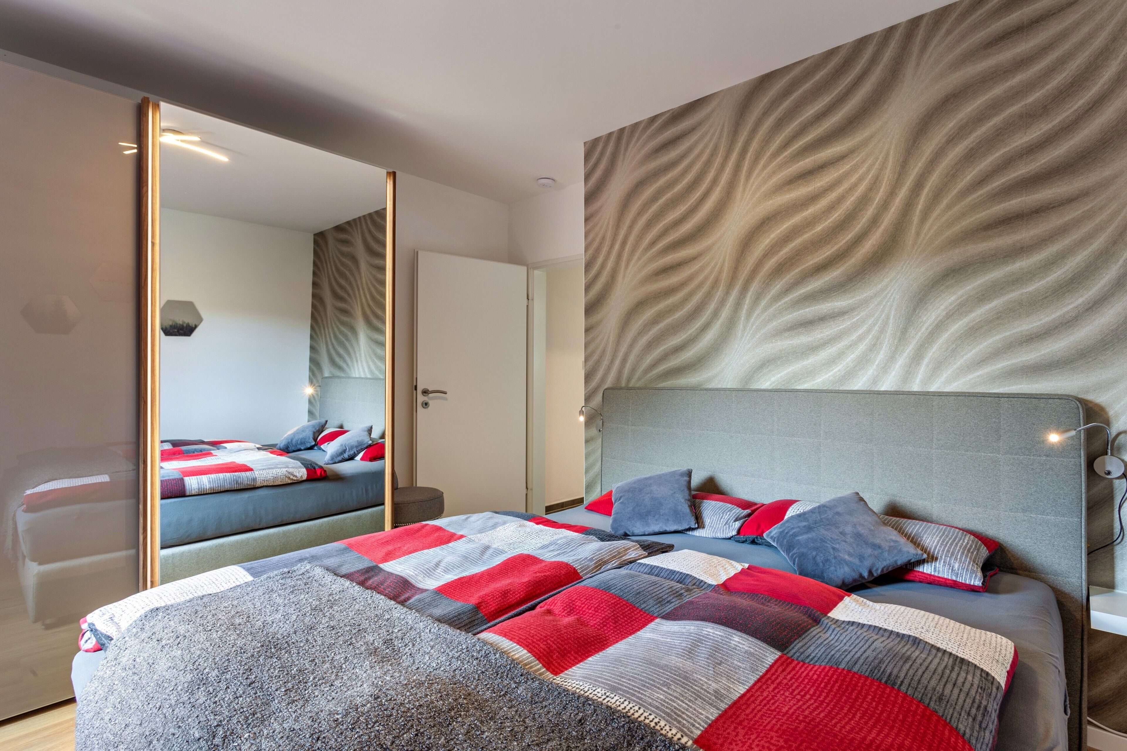 A bedroom with a bed, a mirror, and a textured wall.