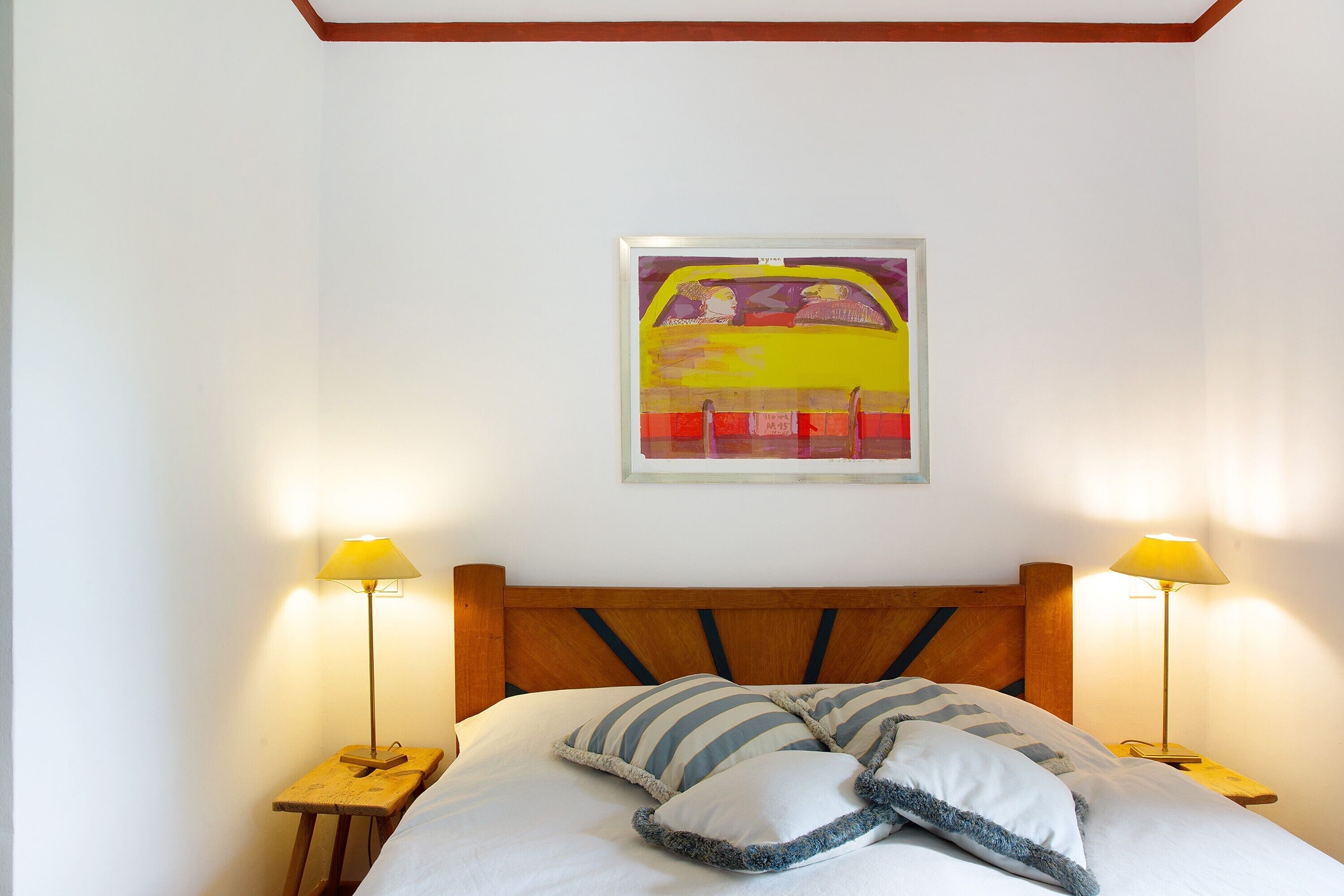 Un letto con testiera in legno, due lampade sui comodini e un quadro appeso al muro.