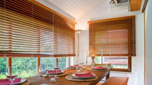 A dining area with a wooden table set for a meal, large windows with blinds, and a view of greenery outside. - Holiday Home 'Ferienhaus Auszeithaus' with Private Terrace, Private Garden and Wi-Fi (Zell/Ebenhausen)