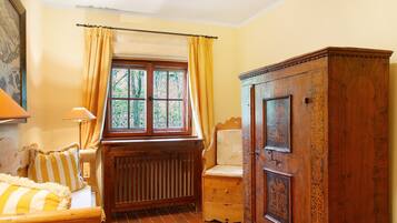 Quarto com radiador de madeira, janela com cortinas amarelas, armário de madeira e cama com roupa de cama listrada.