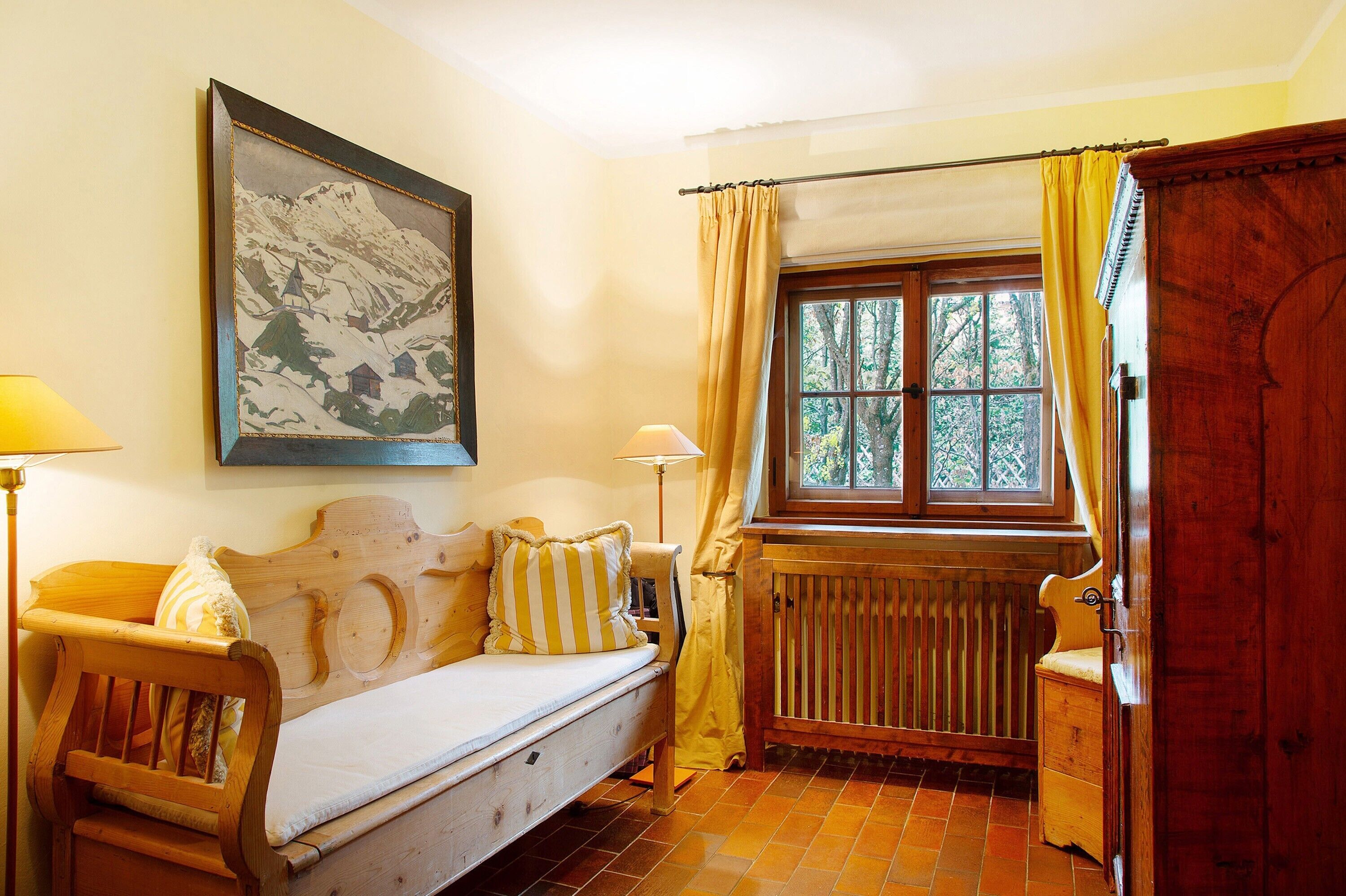 Ein gemütliches Zimmer mit einer hölzernen Bank, einem Heizkörper, einem fenster mit Vorhängen und einem gerahmten Bild an der Wand.