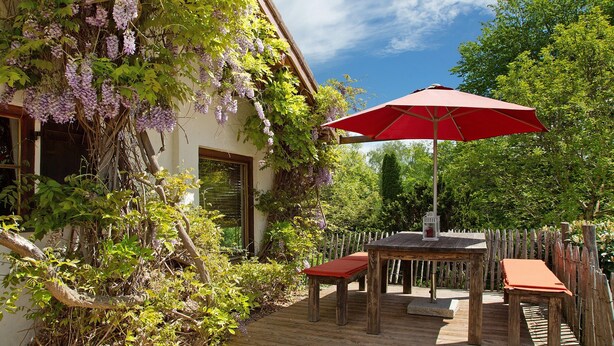 A wooden deck with a table and chairs, a red umbrella, and a house with climbing plants. - Holiday Home 'Ferienhaus Auszeithaus' with Private Terrace, Private Garden and Wi-Fi (Zell/Ebenhausen)
