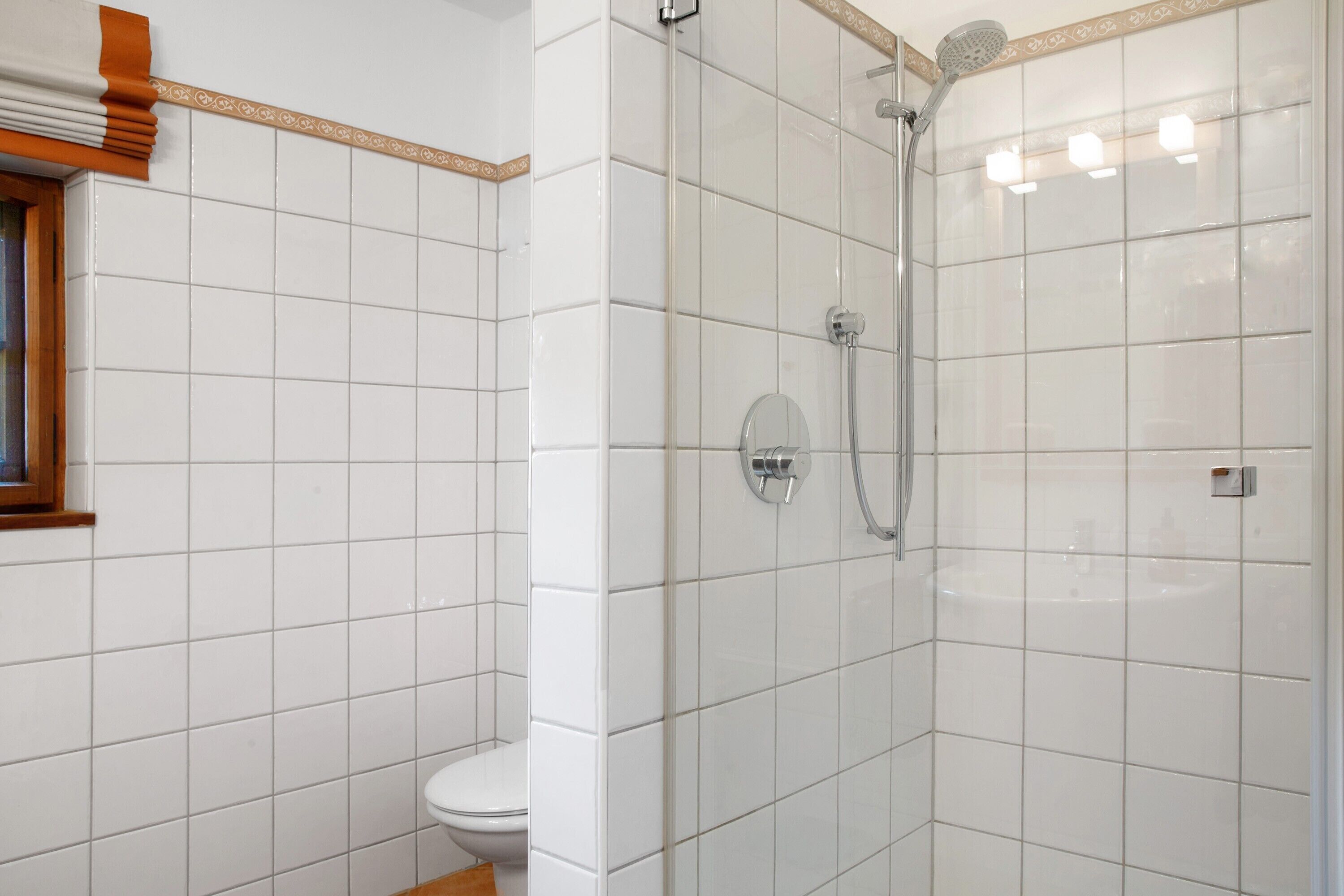 A bathroom with white tiled walls, a shower with a glass door, and a toilet.