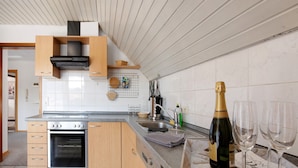A modern kitchen with wooden cabinets, a built-in oven, a stainless steel sink, and a wine bottle with glasses. - Apartment 'Ferienwohnung Lange' with Mountain View, Balcony and Wi-Fi (Waldstetten)