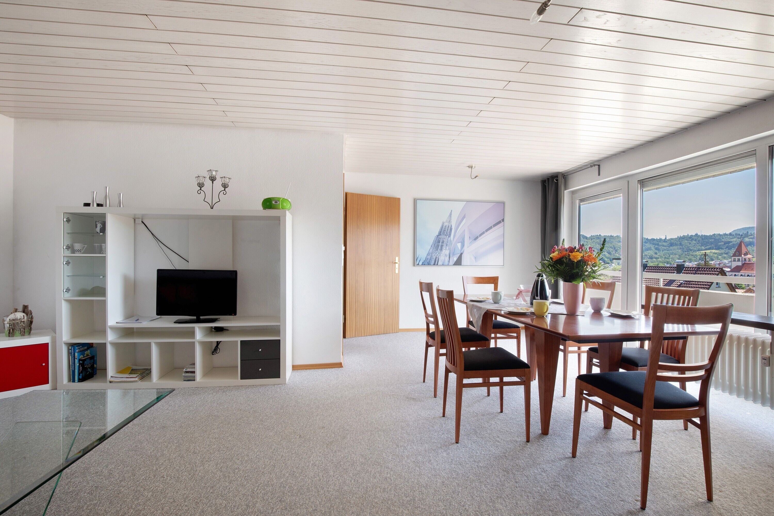 A modern living room with a TV, dining area, and large windows with a view.