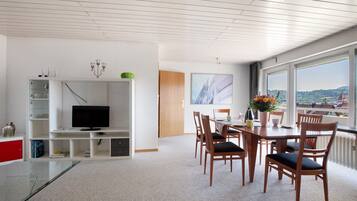 A modern living room with a TV, dining area, and large windows with a view.