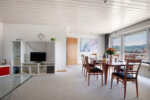 A modern living room with a TV, dining area, and large windows with a view. - Apartment 'Ferienwohnung Lange' with Mountain View, Balcony and Wi-Fi (Waldstetten)