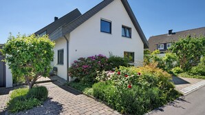 A modern house with a sloped roof, a paved driveway, and a well-maintained garden with various plants and flowers. - Apartment 'Ferienwohnung Lange' with Mountain View, Balcony and Wi-Fi (Waldstetten)