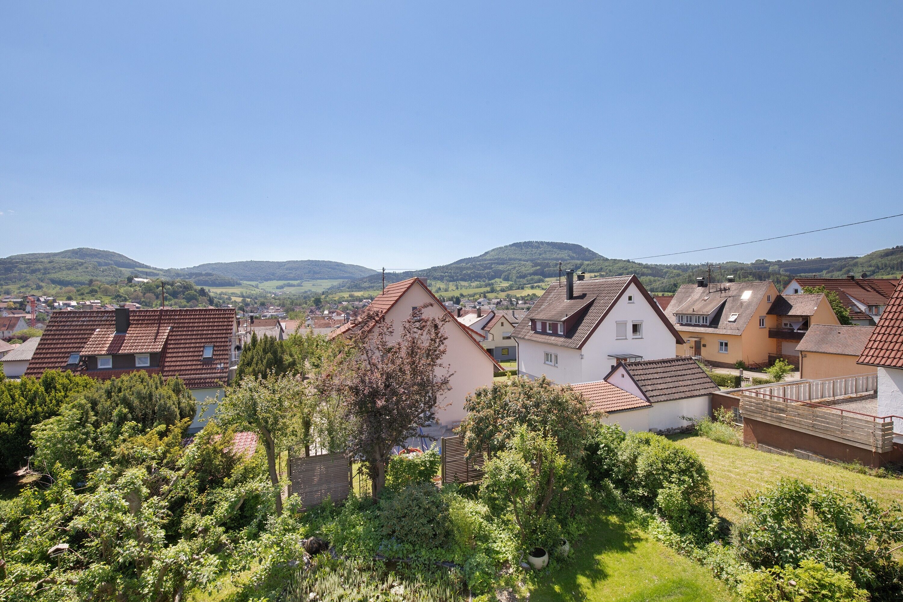 Un quartier résidentiel avec des maisons, des arbres et un paysage vallonné en arrière-plan.