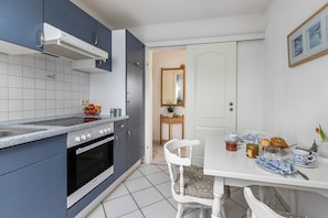 A modern kitchen with a stove, oven, and sink, a dining table with plates and cups, and a chair.