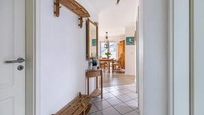 Un pasillo con un banco de madera, una puerta con manija, un espejo y una zona de comedor al fondo.