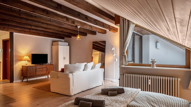 Ein modernes Wohnzimmer mit einer Couch, einem Fernseher, einem Schrank und einem Fenster mit Vorhängen.