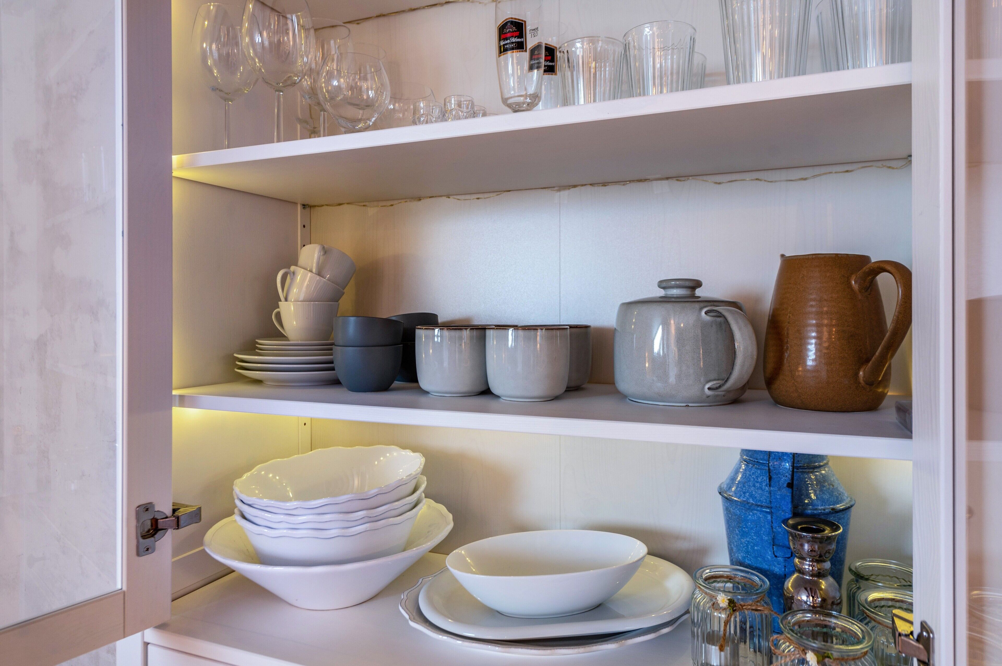 A kitchen with white cabinets, shelves with glassware, bowls, and jars.