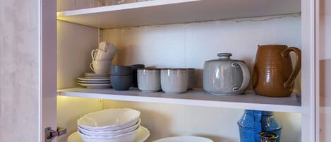 A kitchen with white cabinets, shelves with glassware, bowls, and jars.