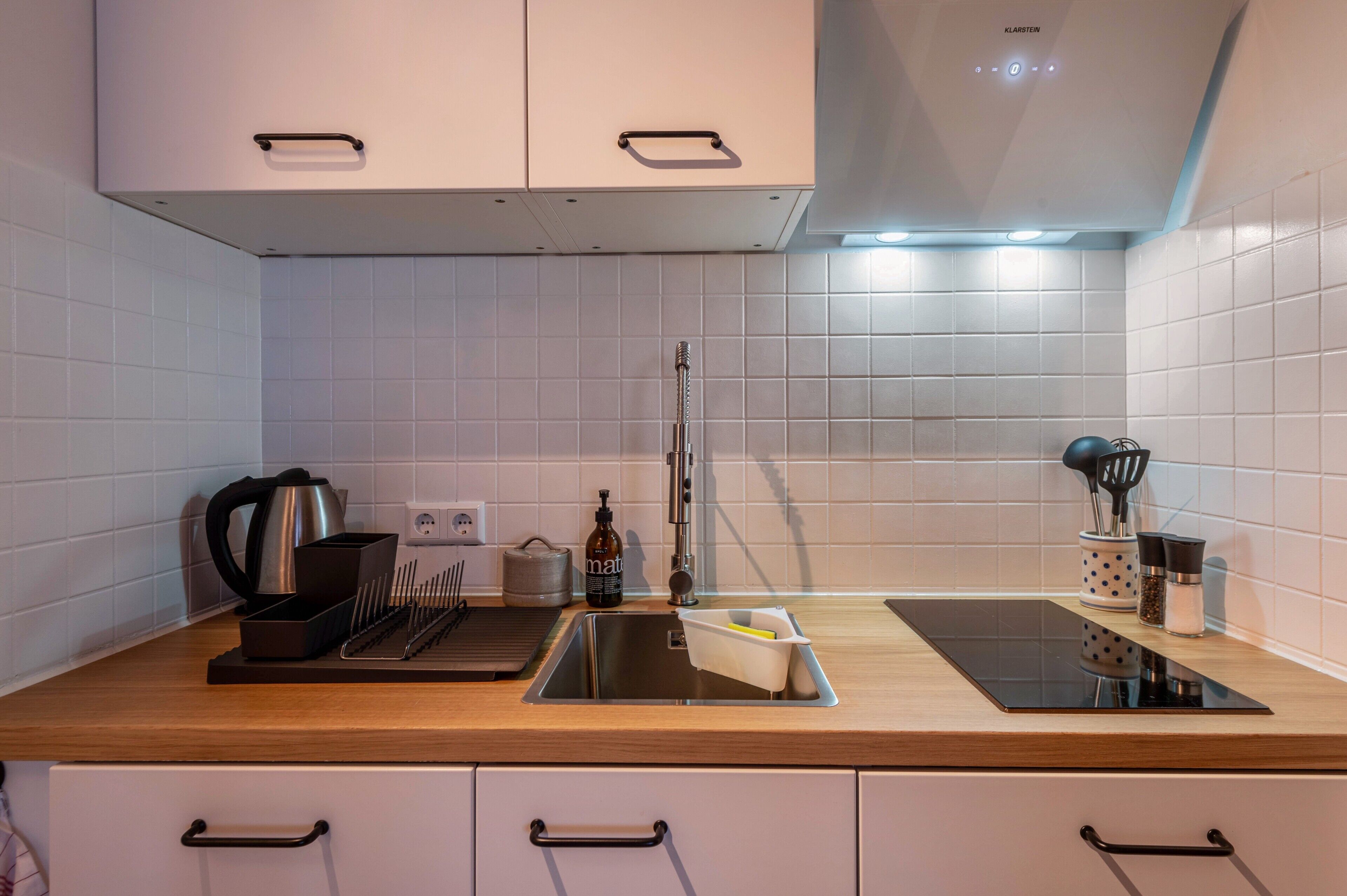 A modern kitchen with white cabinets, a stainless steel sink, and a wooden countertop.