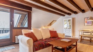 Ein gemütliches Schlafzimmer im Loft-Stil mit schrägem Dach, einer Couch mit gemusterten Kissen, einem Holztisch und einer weißen Kommode.