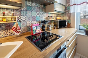 A modern kitchen with a black induction cooktop, wooden cabinets, a microwave, and a tiled backsplash.