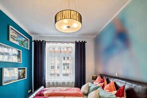 A bedroom with a bed, a window with curtains, a ceiling light, and wall art.