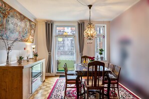 A dining area with a table set for four, a chandelier, and a view through a window.
