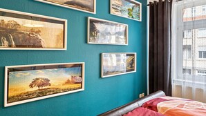 Une pièce aux murs de couleur turquoise, un lit avec une literie rouge et orange, et plusieurs tableaux encadrés accrochés au mur.