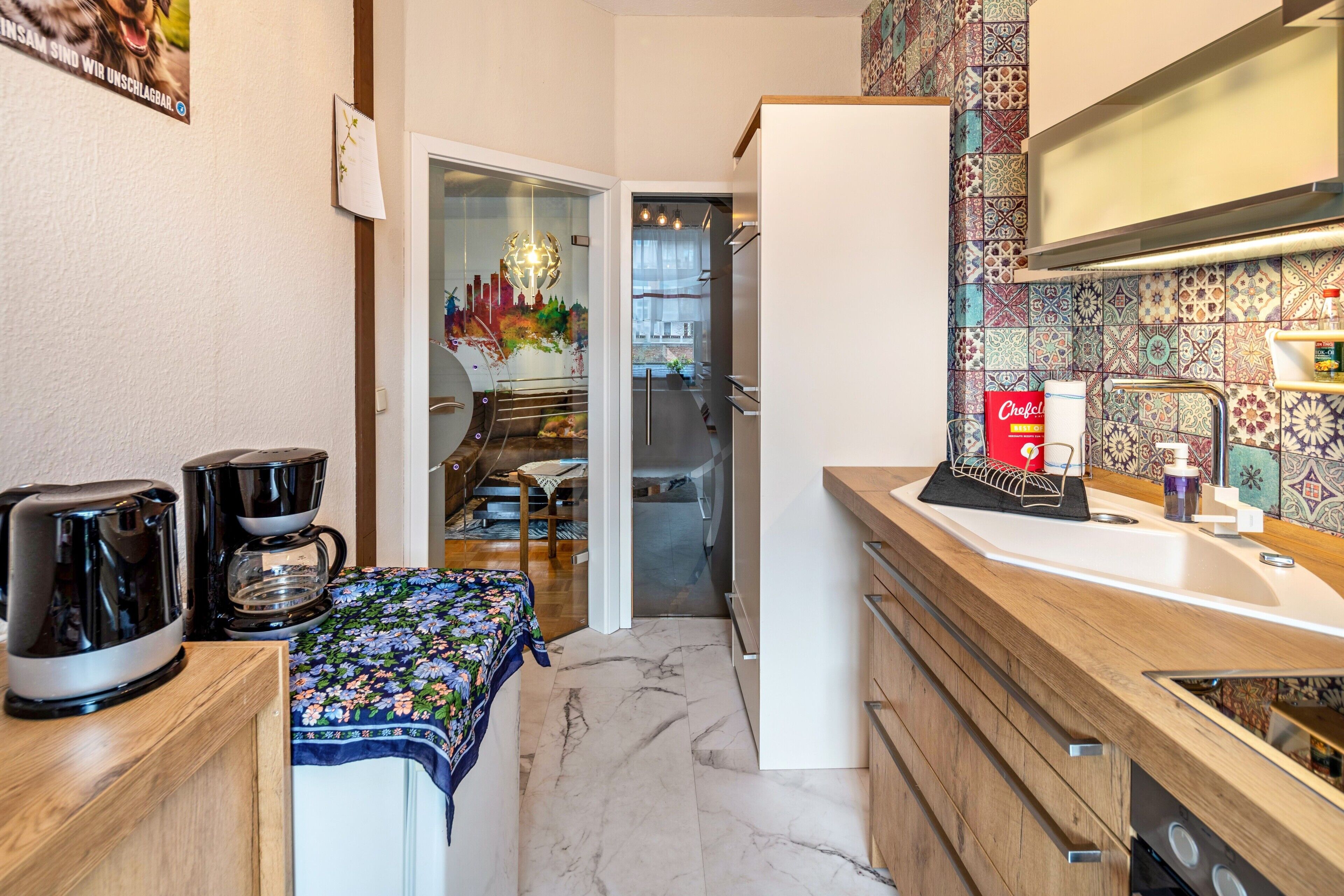 Una cucina compatta con macchina da caffè, frigorifero, lavello e schienale decorato.