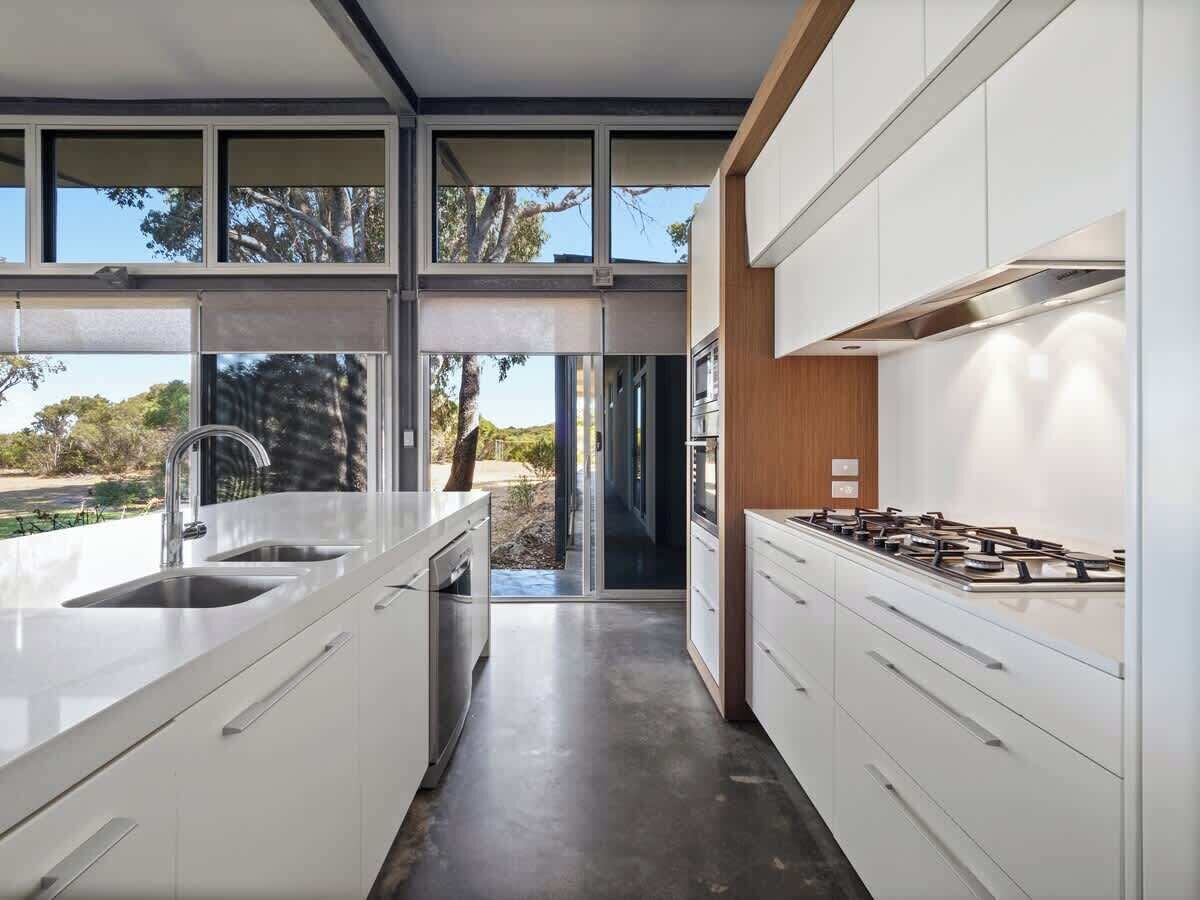 Une cuisine moderne avec des meubles blancs, une cuisinière à gaz et une grande fenêtre donnant sur un paysage naturel.