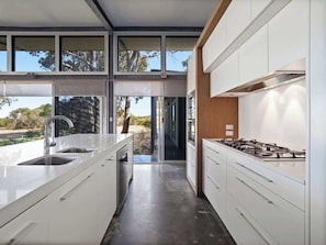 A modern kitchen with white cabinetry, a gas stove, and a large window overlooking a natural landscape.