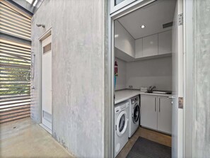 A compact laundry room with a washing machine, a sink, and cabinets.