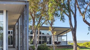 A modern house with large windows, a covered outdoor area, and trees in the yard.