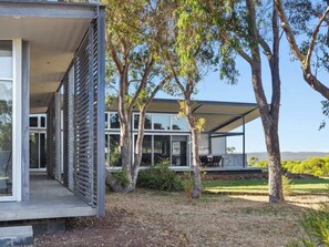 A modern house with large windows, a covered outdoor area, and trees in the yard.