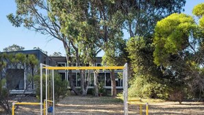 A playground with yellow and white equipment, surrounded by trees and a building in the background.