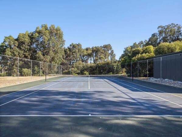 An outdoor tennis court with a net, surrounded by trees and a fence.