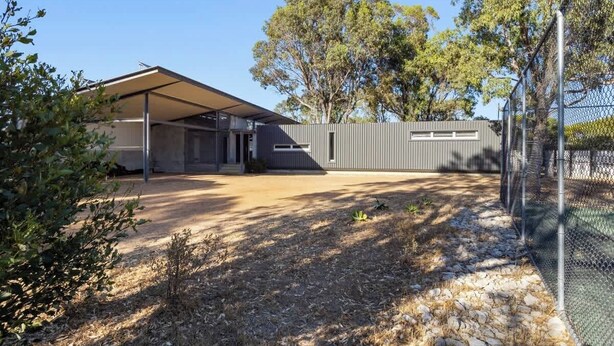 A modern house with a covered patio, a fenced yard, and a clear sky.