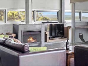Una sala de estar moderna con chimenea, asientos cómodos y ventanas amplias con vistas al exterior.