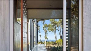 A modern hallway with glass doors leading to a view of trees and the ocean.