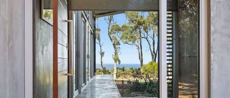 A modern hallway with glass doors leading to a view of trees and the ocean.