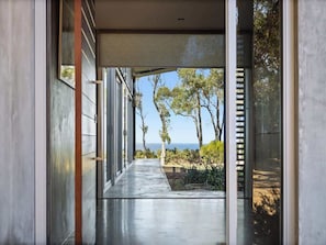 A modern hallway with glass doors leading to a view of trees and the ocean.