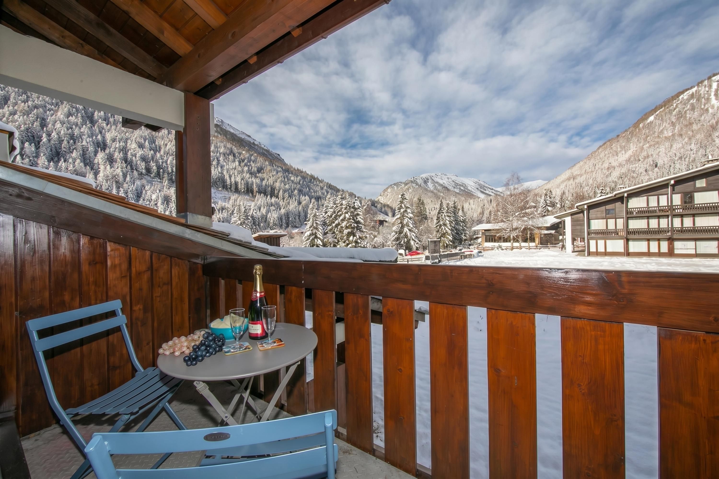 Un balcon avec une table et des chaises, donnant sur un paysage montagneux enneigé.