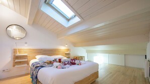 A modern bedroom with a skylight, wooden floor, and a neatly made bed with towels and flowers.
