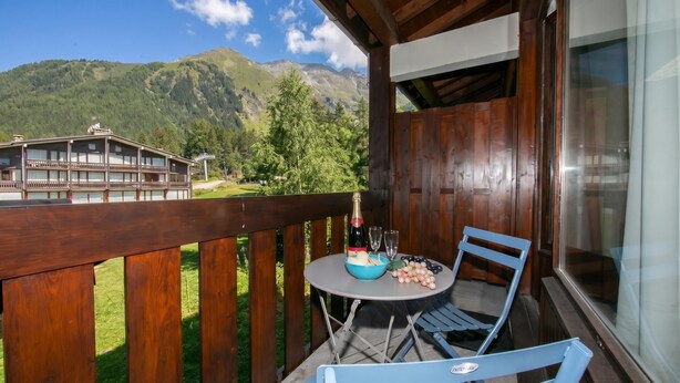 A wooden balcony with a table, chairs, and a bottle of champagne.