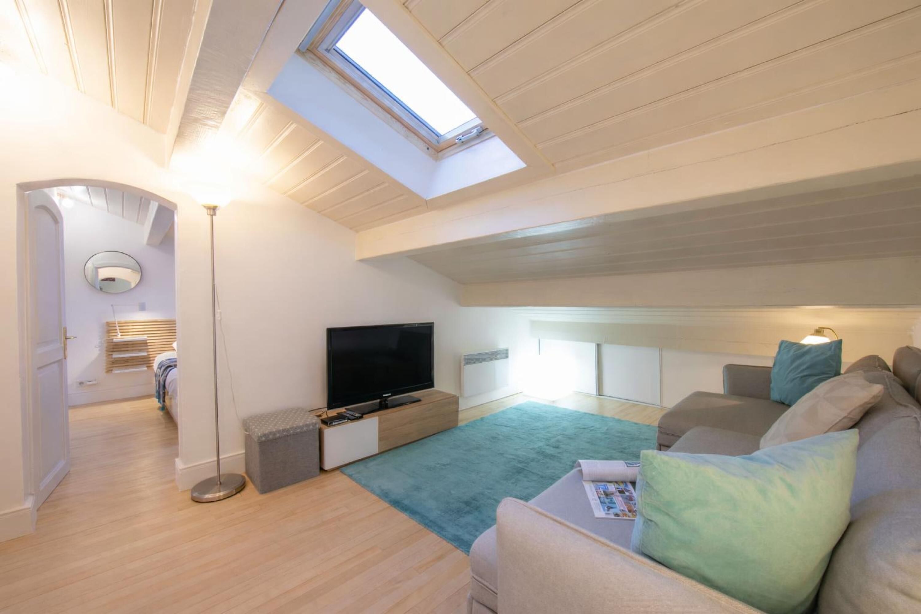 A modern loft bedroom with a skylight, a flat-screen TV, a sofa, and a bedside table.