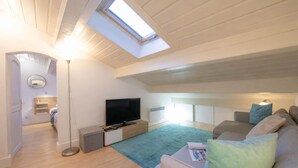 A modern loft bedroom with a skylight, a flat-screen TV, a sofa, and a bedside table.