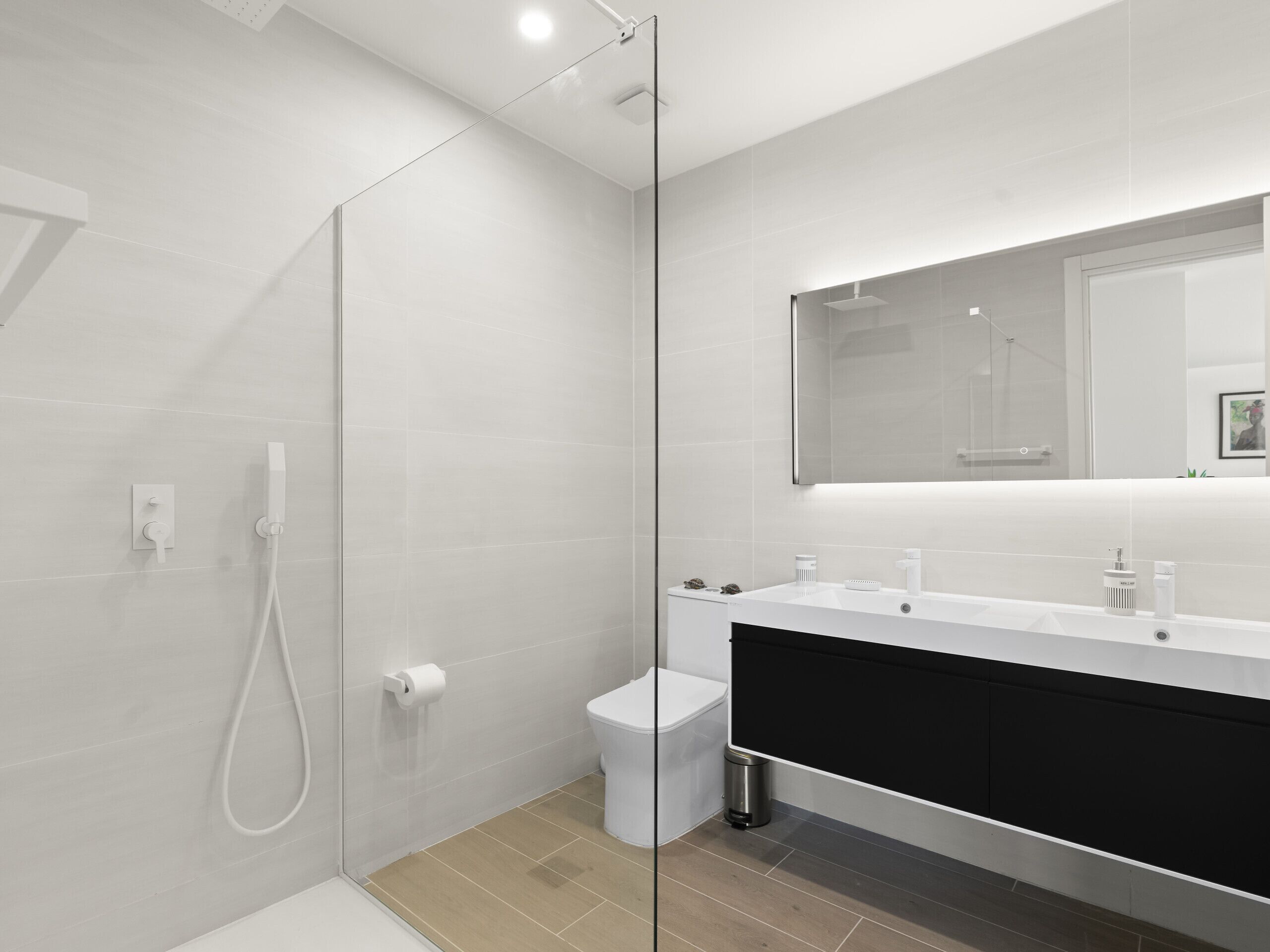 A modern bathroom with a glass shower enclosure, a white sink with a black cabinet, and a large mirror above the sink.